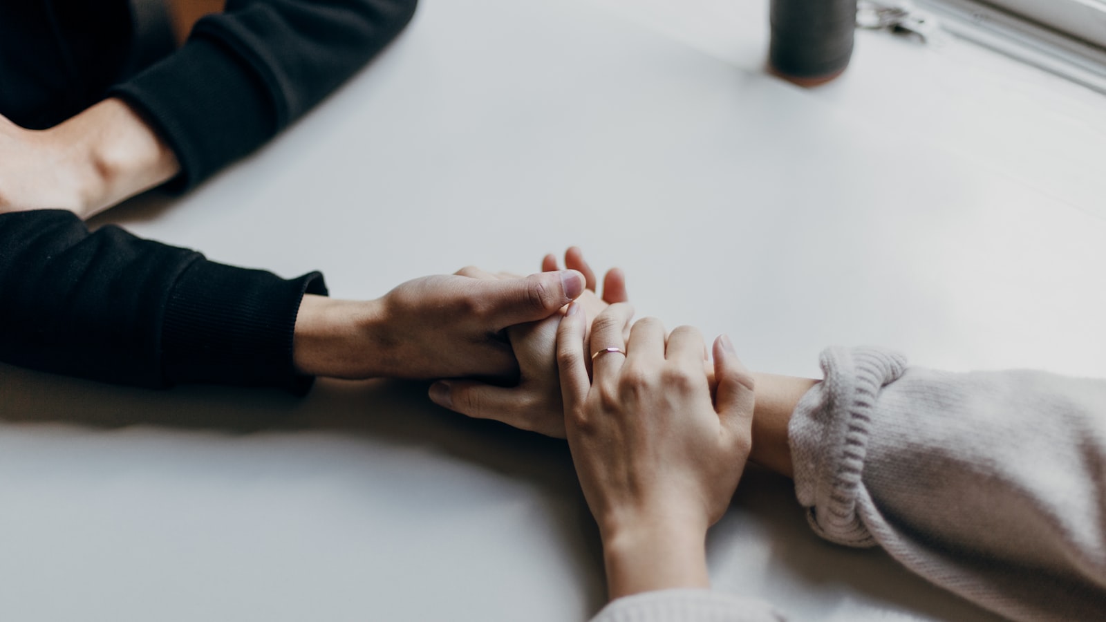 Two pairs of hands resting together on a wooden table