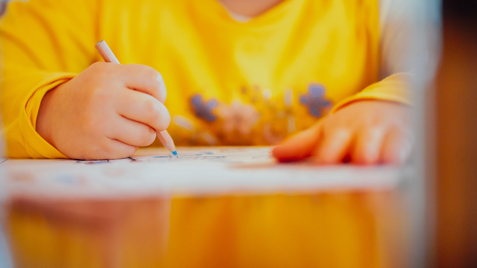 A child's hands colouring on paper at a table
