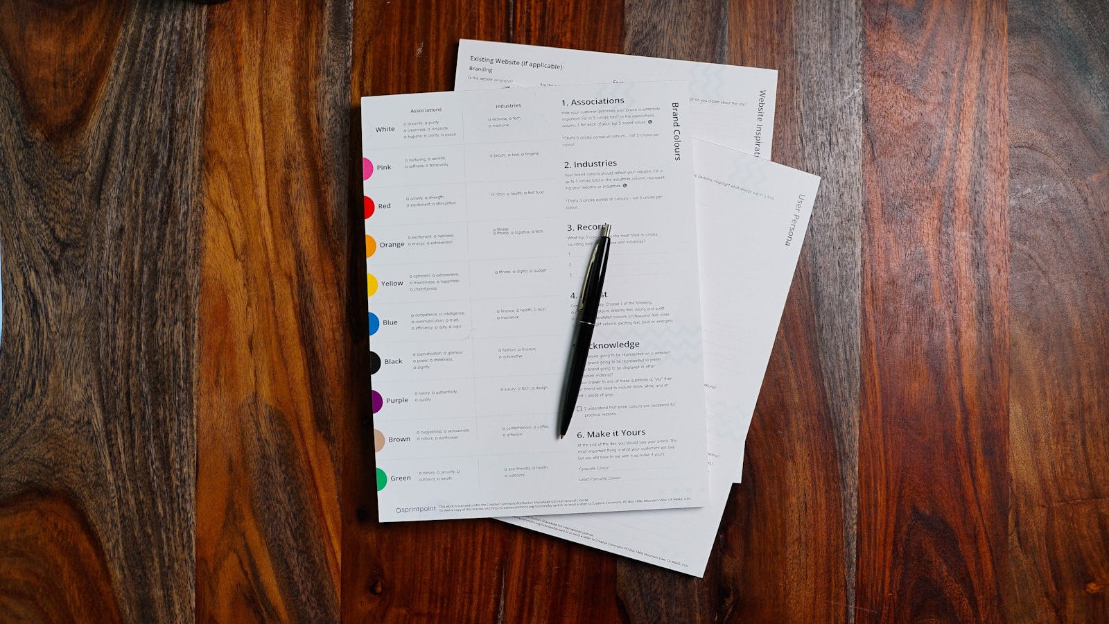 A stack of printed documents on a desk beside a pen