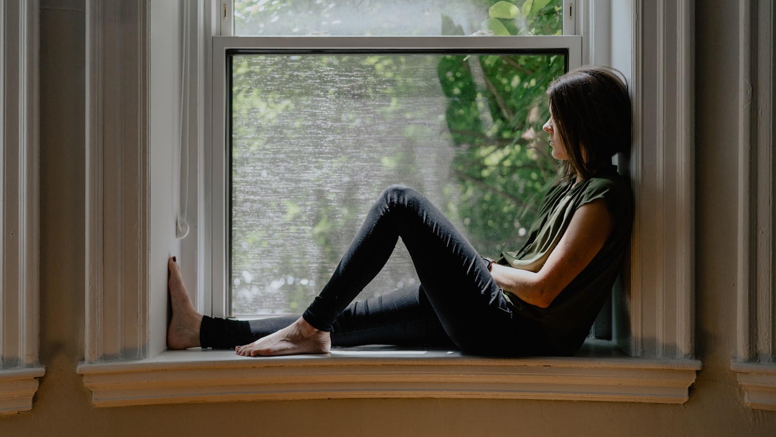 A pregnant person sitting quietly beside a window