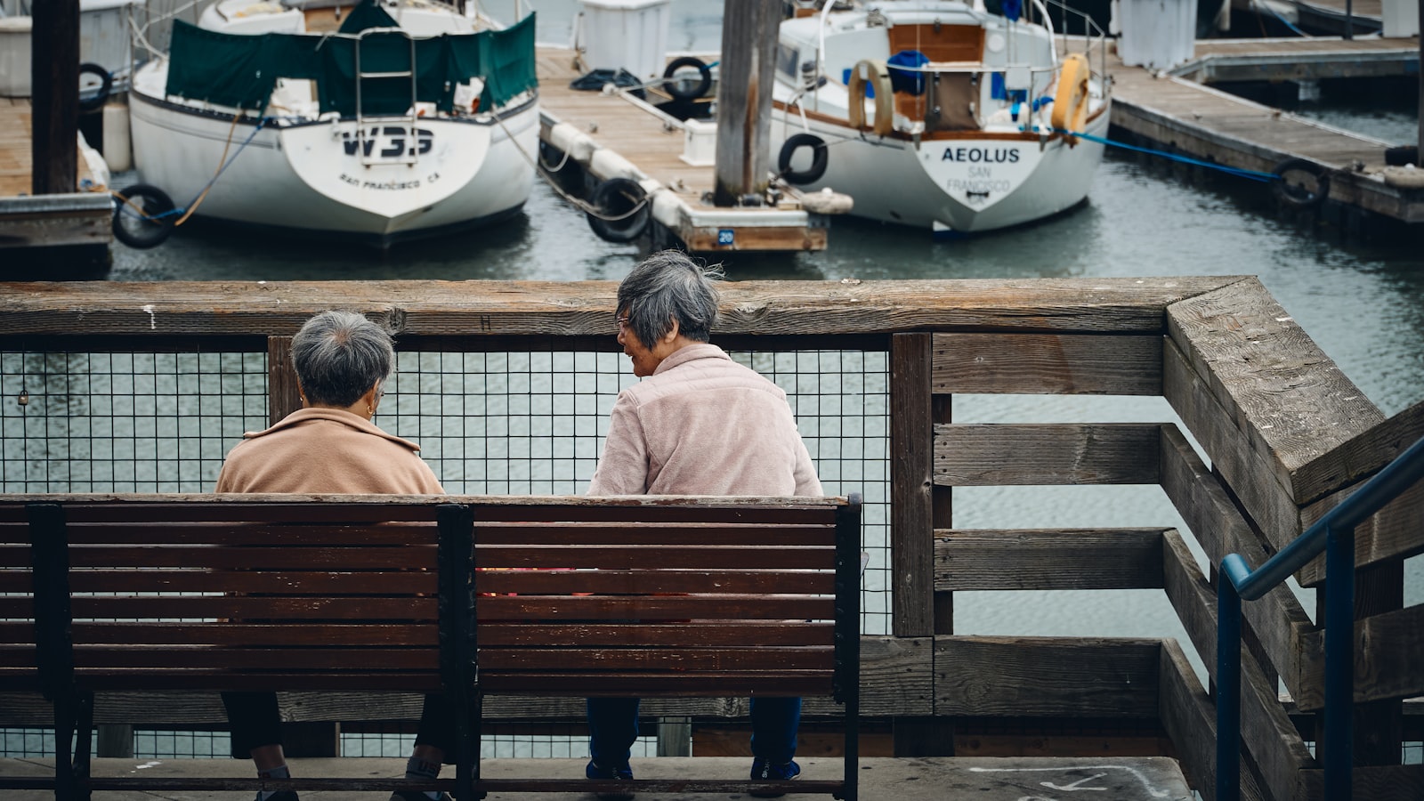 An older person sitting alone on a park bench looking away