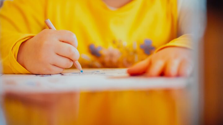 A child's hands colouring on paper at a table