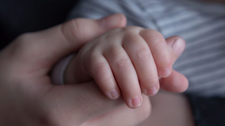 An adult hand gently holding a baby's hand