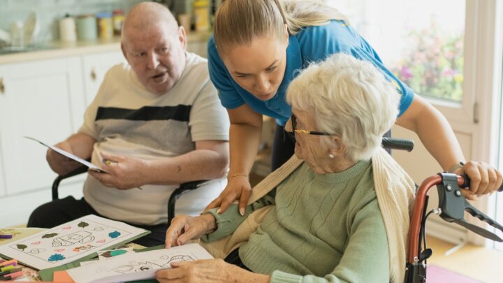 A younger adult helping an older woman read through paperwork at a table
