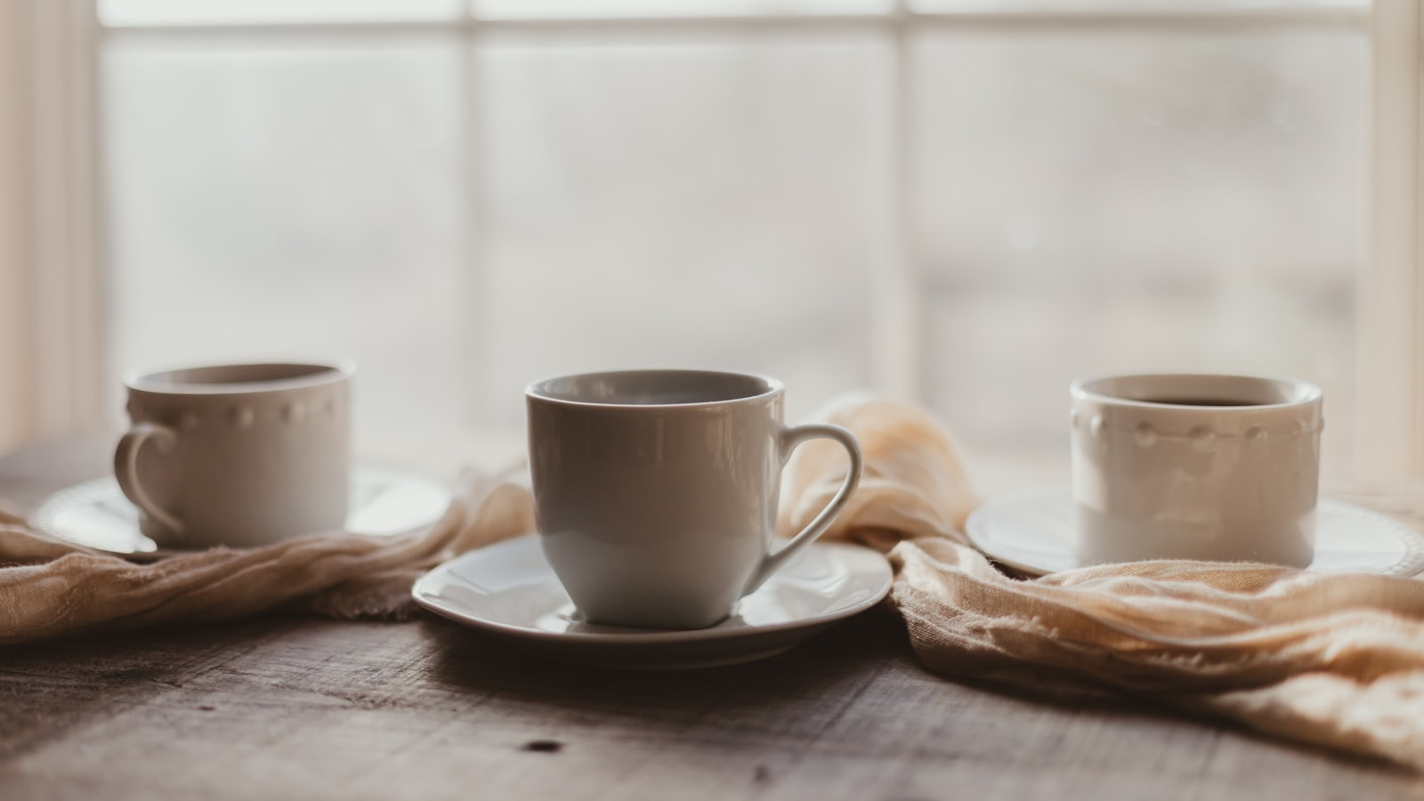 Two coffee cups on a table beside a window