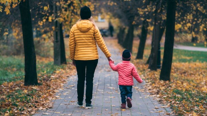 An adult and a child walking together holding hands, seen from behind