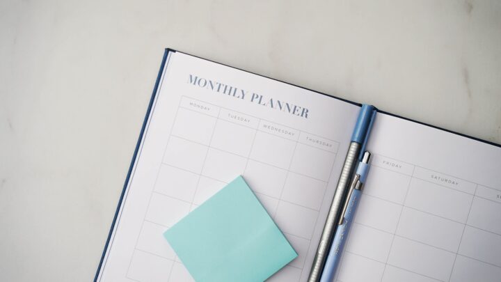A desk planner and pen beside a cup of coffee