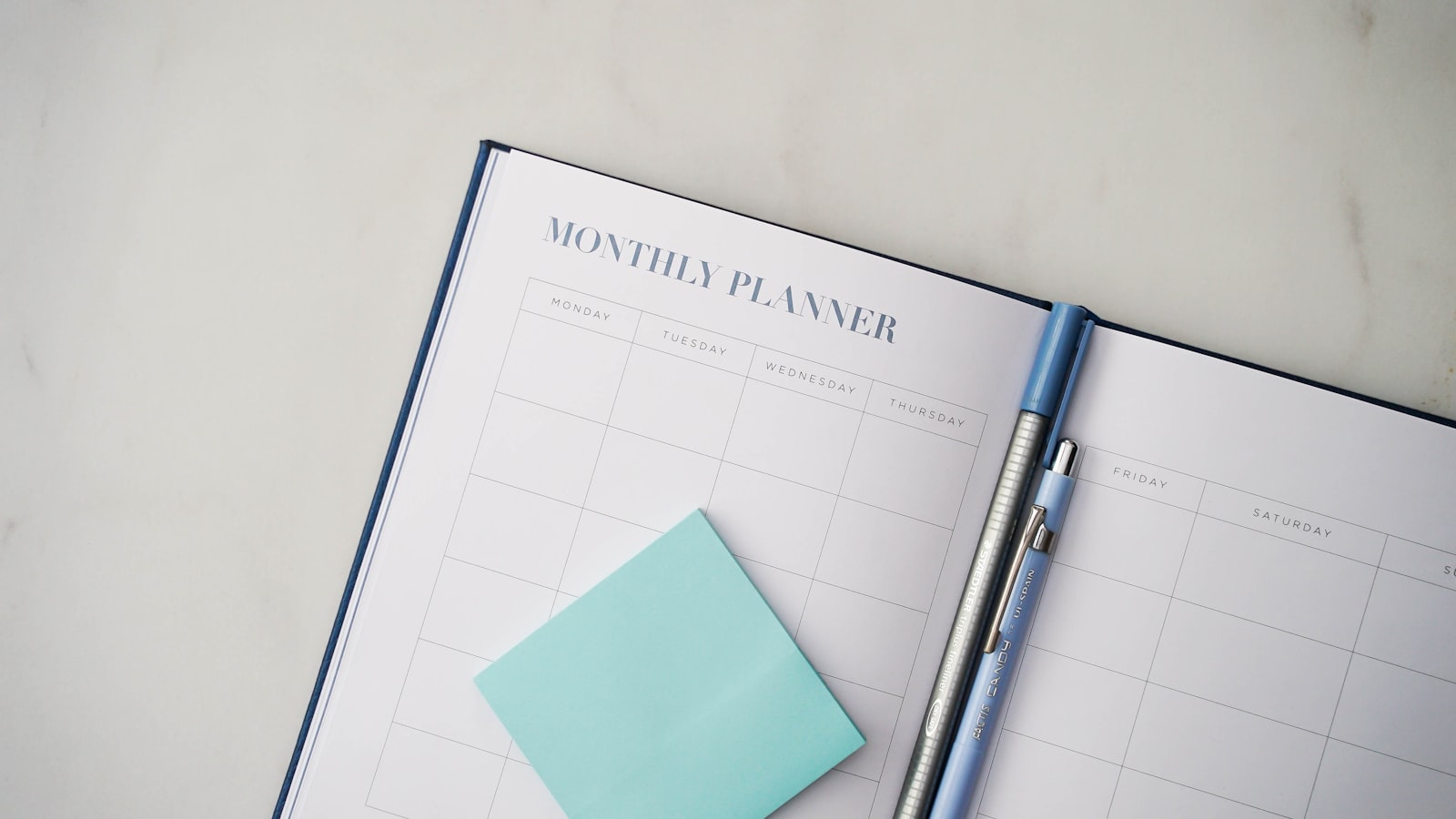 A desk planner and pen beside a cup of coffee
